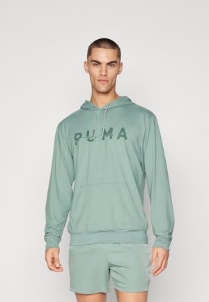 Gai zaļš kapucis ar elastīgām aprocēm un regulējamu kapuci. Uz priekšpuses ir liels, izbalējis "PUMA" logotips.
