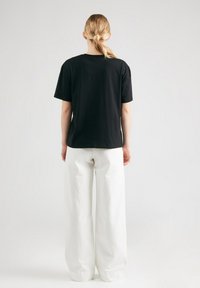 Zwarte katoenen T-shirt met een casual pasvorm, korte mouwen en ronde halslijn, gecombineerd met brede witte broeken gemaakt van textuurstof.