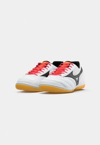 White athletic shoes with black accents, red laces, and orange tongue. Features textured material and gum rubber sole.