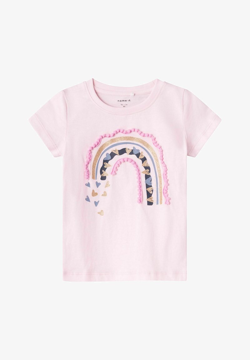Camiseta de manga corta en color rosa claro, con un diseño de arco iris multicolor adornado con flecos de pompones y acentos en forma de corazón en varios colores.