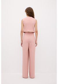 Roze crop-top zonder mouwen gecombineerd met hoge taille, wijde broek. De stof heeft een soepele textuur en een schone, eenvoudige snit.