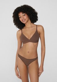 Braun nahtloser BH mit einem flachen V-Ausschnitt, dünnen verstellbaren Trägern und passendem braunem Bikini-Höschen mit minimalem Bund. Weicher Stoff mit angenehmer Textur.