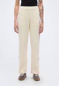 Φόρμες σε κρεμ απόχρωση με φαρδιά γραμμή, ελαστική μέση και πλαϊνές ρίγες. Μαλακό ύφασμα με λεία υφή.