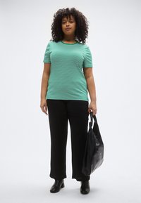 Žaliai baltų dryžių marškinėliai su apvalia iškirpte, derinami su juodomis plačiomis kelnėmis. Kiti akcentai – juoda pintinė rankinė ir aulinukai.