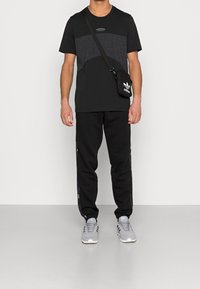 Černé tričko s šedým panelem, v kombinaci s černými tepláky se bočními akcenty. Šedé tenisky a malá černá kabelka přes rameno jsou součástí.