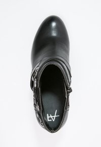 Czarne skórzane botki za kostkę z okrągłym noskiem, bocznym zamkiem i łańcuszkiem ozdobnym wokół kostki, co dodaje tekstury.