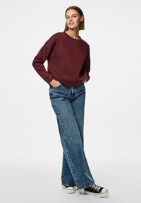 Burgunderfarget genser med rund hals, avslappet passform og ribbestrikkede mansjetter, kombinert med vide blå denimjeans og svarte kanvas-sneakers.