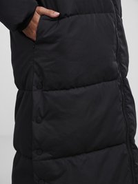 Black puffer coat with horizontal quilted panels, featuring a zip closure and side pockets. Smooth fabric with a matte finish.