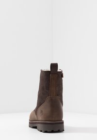 Stivale alla caviglia in pelle marrone con parte superiore in suede, tacco rinforzato e suola in gomma. Presenta un tassello sul retro e un dettaglio del logo sul lato.