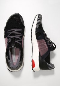 Czarne i szare dziane buty sportowe z białymi podeszwami i różowymi siateczkowymi bokami, pokazane z widoku z góry i z boku na białym tle.