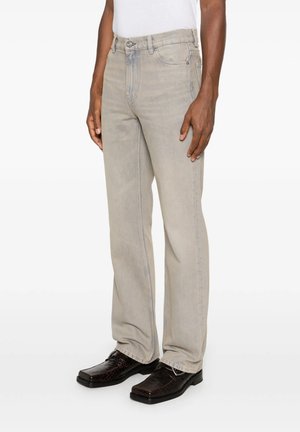 Uomo con jeans beige chiaro a gamba dritta con bottoni e zip e scarpe eleganti marrone scuro con punta quadrata.