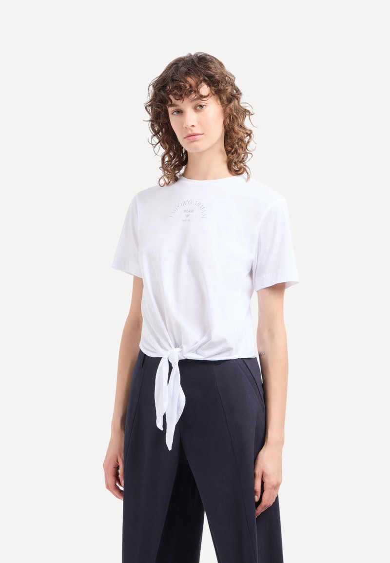 Witte katoenen t-shirt met een geknoopte voorkant. Korte mouwen en ronde halslijn, met een subtiele grafische print op de borst.