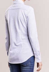 Light gray long-sleeve shirt with a collar, featuring a buttoned cuff and a curved hem. Made from soft fabric with a subtle texture.
