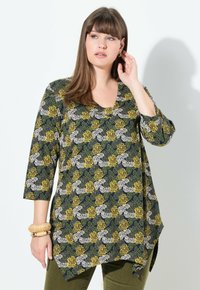 Top con motivo floreale su sfondo blu navy, con fiori gialli, bianchi e verdi. Scollatura a V, maniche a tre quarti e orlo asimmetrico.