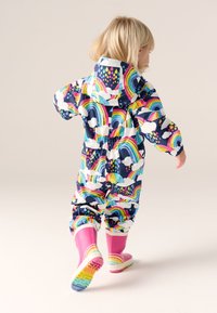 Colorful raincoat featuring a navy base with rainbow and cloud patterns, elastic cuffs, hood, and pink rubber boots with rainbow accents.
