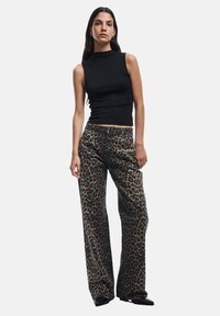 Top negro sin mangas combinado con pantalones anchos de estampado de leopardo. La tela tiene una textura suave con un atrevido patrón animal y tonos neutrales.
