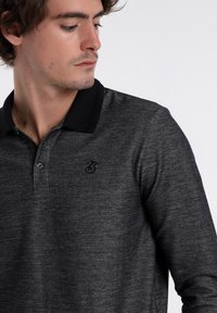 Schwarz-graues langärmeliges Poloshirt mit Kragen und einer Drei-Knopf-Leiste, das ein dezentes Logo auf der Brust trägt.