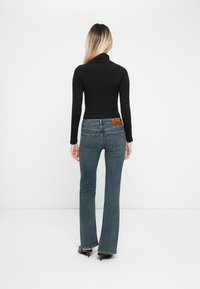 Svart langermet topp kombinert med blå flare jeans med et brunt lærmerke og to baklommer. Glatt tekstur.