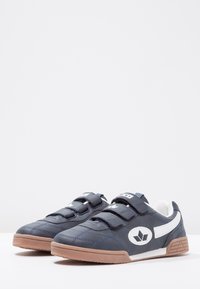 Chaussures synthétiques bleu marine avec des accents blancs, des brides auto-agrippantes et des semelles en caoutchouc beige. Avec un bout arrondi et une finition lisse.