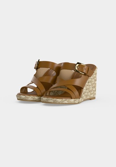 Sandales compensées en cuir marron avec brides croisées, boucle dorée et talons compensés en jute tressée, présentées sur fond neutre.
