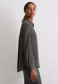 Black blouse with a floral pattern, long sleeves, and a button-up collar. Lightweight fabric with a slightly relaxed fit and curved hem.