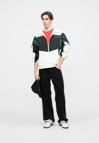 Baltas un melns vējjakas ar zaļiem akcentiem, sarkans krekls, melnas džinsus un baltas tenisa apavus. Neformāla piegriezne, gluda auduma un relaksējošs dizains.