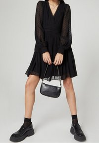 Svart klänning med prickar, långa puffärmar och insydd midja; matchad med en liten, strukturerad svart handväska och plattformsskor.