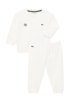 Ensemble blanc composé d'un haut à manches longues et d'un pantalon avec des logos crocodile Lacoste verts et un écusson du tournoi Roland Garros sur le haut.