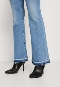 Jean évasé taille haute bleu clair avec ourlet effiloché, associé à des escarpins noirs à bout pointu en cuir lisse.