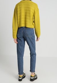 Pull court jaune avec des rayures texturées, associé à un jean bleu taille haute et des baskets noir et gris avec des accents jaunes.