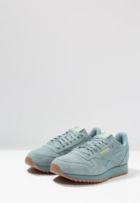 Ljusa blå mockaskor för sport med en texturerad ovandel, gummisula och gröna accenter. Har snörning och sidologga.