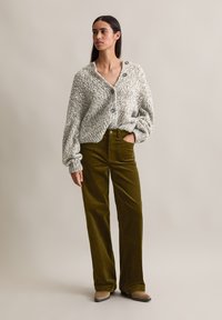 Cárdigan de punto gris grueso con grandes botones, combinado con pantalones de pana verde olivo de cintura alta. Textura suave, corte relajado y piernas anchas.