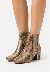 Snakeskin-patterned ankle boots with a rounded toe and block heel, featuring a combination of beige and black colors in a textured finish.