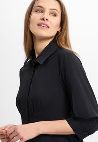 Black, lightweight shirt with a buttoned collar, three-quarter sleeves, and subtle texture. Features a central button placket.