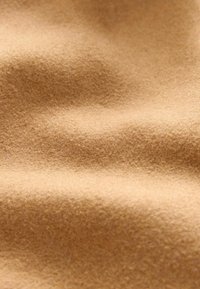 Tela de fieltro color beige que muestra una superficie suave y texturada con sutiles ondulaciones y un brillo constante, destacando su naturaleza ligera y flexible.