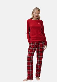 Top rojo de manga larga acompañado de pantalones de cuadros rojos con líneas negras y blancas. Tejido suave con un ajuste relajado. Sin hardware visible.