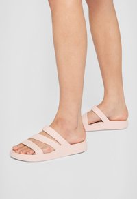 Jasnoróżowe klapki z trzema poziomymi paskami. Wykonane z gładkiego materiału, z niskoprofilową podeszwą i otwartym noskiem.