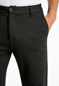 Sorte bukser lavet af glat stof har et tætsiddende design med knaplukning og sidelommer. Detaljerede syninger forbedrer det samlede udseende.