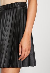 Gonna plissettata nera realizzata in materiale sintetico, con una texture liscia e una vita. Le pieghe sono uniformemente distribuite e ben definite.