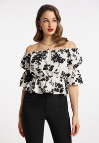 Blumenoff-Shoulder-Bluse in Weiß und Schwarz mit puffigen Ärmeln, Rüschensaum und elastischem Bund. Kombiniert mit schwarzer, taillierter Hose.