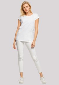 White cotton t-shirt with rolled short sleeves, paired with white fitted jeans and white sneakers, set against a neutral background.