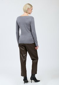 Maglione grigio lavorato a maglia con scollatura ampia, abbinato a pantaloni in ecopelle marroni. È visibile il tessuto testurizzato e i dettagli di design aderenti.