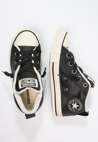 Czarne skórzane wysokie trampki z białymi gumowymi nosek i puszystym wykończeniem. Posiadają czarne sznurowadła, naszywkę z logo oraz białe paski na podeszwie.