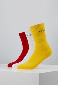 Drei Paar gerippte Socken: rot, weiß und gelb. Jede Socke hat eine einfarbige Optik mit Text am Schaft. Glatte Textur, wadenlang.