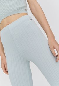 Leggings côtelés bleu clair à taille haute et design sans coutures. Présentent une texture lisse et un accent subtil de la marque près de la ceinture.