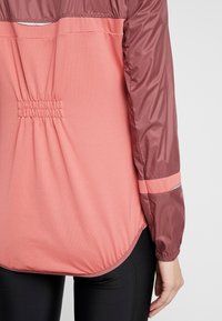 Lettermaterialet letvægts to-farvet jakke med en pink krop og burgunder ærmer, med en indsnævret ryg, glat tekstur og reflekterende detaljer.