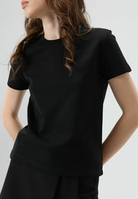 T-shirt noir à manches courtes en coton, avec un col rond et une texture douce. Design simple sans motifs ni accents.