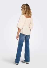 Balti lengvo audinio palaidinė su pūstomis rankovėmis, su raukinukais nugaroje, derinama su blausiai mėlynais plačiomis kojomis džinsais ir sidabrinėmis plokščiais batais.