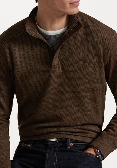 Καφέ πουλόβερ με σχέδιο ψαροκόκκαλο και φερμουάρ μέχρι το ένα τέταρτο, που διαθέτει υφασμάτινη υφή, αποκορυφωμένο με κολάρο σε σκούρο καφέ χρώμα, φορεμένο πάνω από ένα γκρι πουλόβερ.