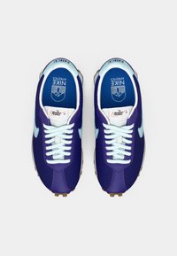 Um par de ténis de corrida Nike em roxo e azul claro com atacadores brancos e palmilhas azuis apresentando o logótipo da Nike Athletics, visto de cima.